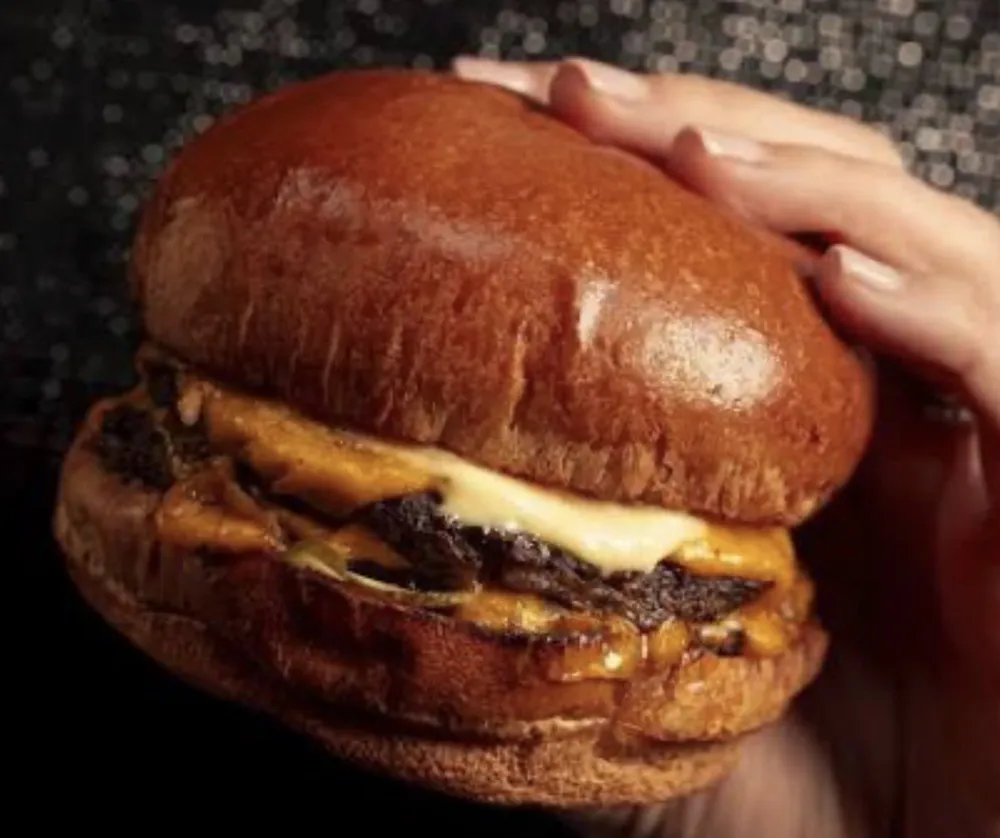 Hamburguesa doble ahumada de Humo en Camino sostenida en la mano, con cheddar derretido